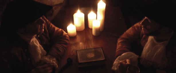 Two men sitting at a table with lit candles. Description generated by AI