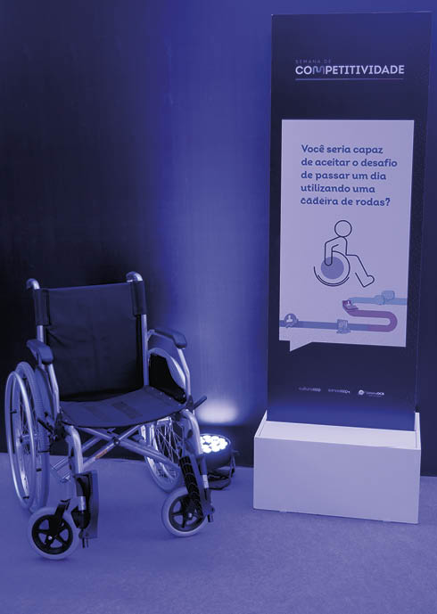 Cadeira de rodas ao lado de um painel com texto em portugu s que desafia o leitor a aceitar o desafio de passar um dia utilizando uma cadeira de rodas. Description generated by AI