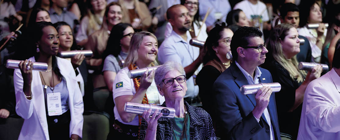 Pessoas em um evento seguram objetos cil ndricos prateados enquanto sorriem e interagem em um ambiente interno com ilumina o suave.  Description generated by AI