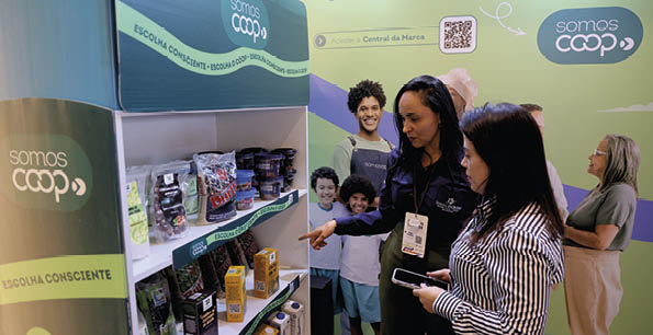 Duas pessoas conversam e apontam para produtos em uma prateleira de supermercado com a marca Somos Coop em um ambiente com decora o verde e azul.  Description generated by AI