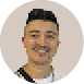 Pessoa adulta com cabelo curto e penteado para cima sorrindo e vestindo camiseta branca com al a preta sobre o ombro, em fundo neutro circular. Description generated by AI