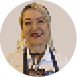 Pessoa adulta sorridente com cabelo preso, usando camisa branca, avental escuro e crach pendurado no pesco o.  Description generated by AI