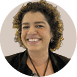 Pessoa adulta com cabelo cacheado curto sorrindo e vestindo roupa preta com colar marrom. Description generated by AI